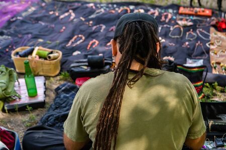 Rear view of vendor of a hand made jewelery stand in local farmers market. Long hair tied up in...