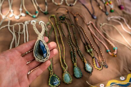 Mans hand holding a hand made necklace with twine string and oval blue stone. Farmers market vendor,...