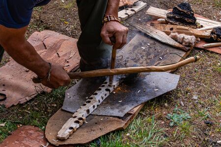 Closeup of man hand holding wooden bow and rope over a wooden piece of burnt holes. demonstrating a...