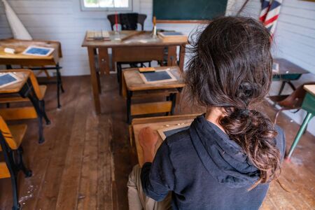 Learning history. Travel to the past century. Young man sitting alone in the empty vintage school class. View from behindの写真素材