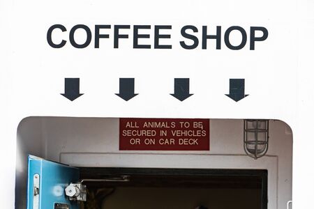Coffee shop sign with black letters painted on white background, on the side of a ferry. Black arrows pointing in the direction of the lower deck.の写真素材