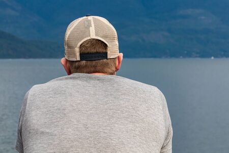 Close up shot from behind of a young man, passenger of a ferryboat navigating in a canadian lake. Passenger looking at landscape near decks railing.の写真素材