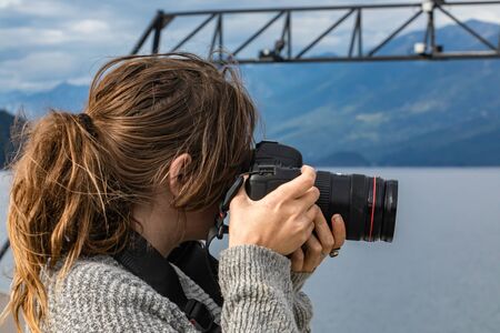 Young woman photographer shot from behind while taking pictures from the deck of a ferry. Expensive photographic equipment and long telephoto lens.の写真素材