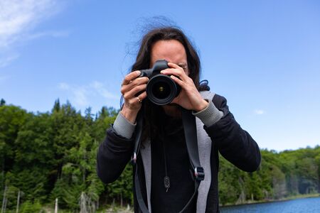 Young american traveler with long hair capturing photos using DSLR camera while riding in lake with fir and spruce trees in Northern Quebec, Canadaの写真素材