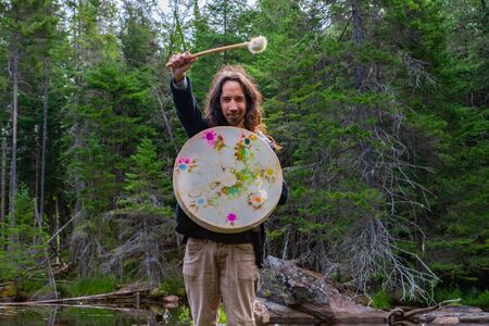 Young american man with long hair holding scared native frame drum and fur covered stick. with hand...
