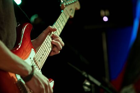 A close up selective focus shot on the hands of a guitar player performing on stage by night at a festival celebrating earth and culture, copy space to rightの写真素材