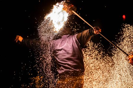 A close up energetic shot of a fire dance performer using a long flaming pole to create flying...
