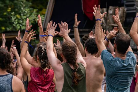 A large group of people are seen from the rear during guided slow moving spiritual dance to heal body and mind, with raised arms during earth festivalの写真素材