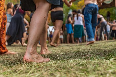 A ground level perspective on the legs of a diverse group of people dancing barefoot on grass during...