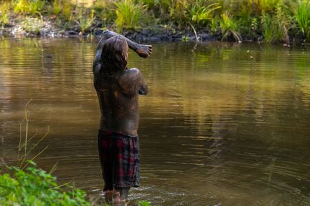 A man is seen bathing in dirty mud water during a forest retreat connecting with nature for healthy...