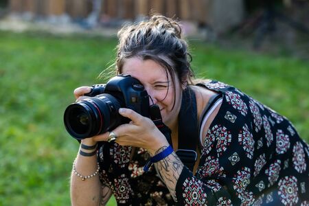 A close up shot of a professional female photographer at work using a digital camera. Behind the lens shot against a blurry grass backgroundの写真素材