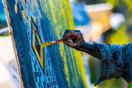 A closeup selective focus shot of a man painting colorful artwork on a canvas. Blue and yellow pattern against a blurry green background, copy space to leftの写真素材