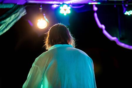A close up view on the back of an electronic musician playing on stage at an earth festival by light, with colorful green and purple lightingの写真素材