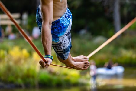 A close up and side view of a slim caucasian man practicing slacklining on a rope anchored over a...