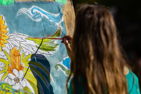 A selective focus shot of an artistic young girl painting on a canvas in nature. on a sunny day at a festival celebrating cultural creatives and earthの写真素材