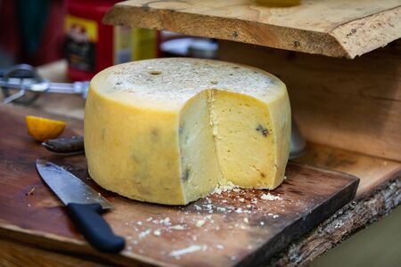 A close up shot on a truckle, wheel, of traditional farmhouse cheddar cheese on a rustic wooden chopping board with large kitchen knife and copy space to rightの写真素材