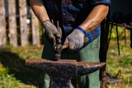 A close up view of a man using a hammer, to work hot metal on a blacksmith anvil during a...