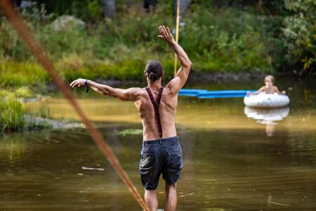 A man is seen from behind with shallow depth of field exercising core muscles walking a slackline in...