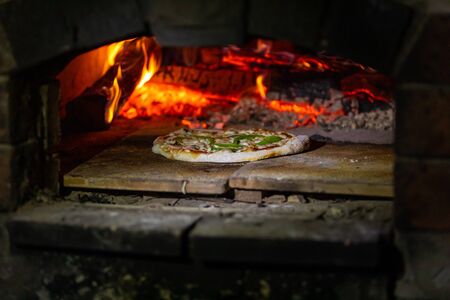 A close up soft focus shot of a traditional wood fired oven, stove cooking fresh handmade pizza at a campsite by night during a multicultural festivalの写真素材