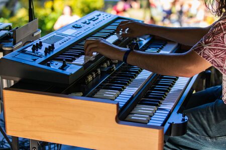 A close up shot of a young man playing an electronic keyboard and synthesizer set on stage at a music festival, blurry audience is seen in backgroundの写真素材