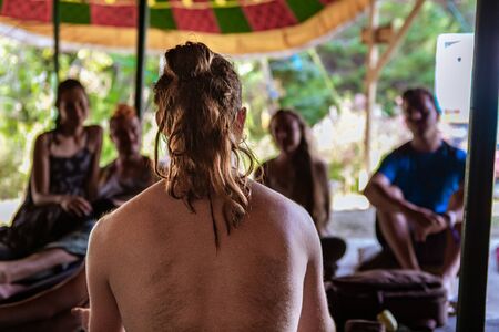 A spiritual teacher is seen from behind with shallow depth of field, talking to a small group of...