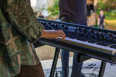 A closeup and cropped shot in selective focus on the hands of a man playing an electronic keyboard synthesizer, with a band on stage at earth festivalの写真素材
