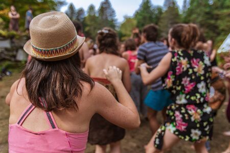A slim caucasian woman wearing pink vest and straw brimmed hat is seen from the rear in selective focus, taking part in group dance at earth festivalの写真素材
