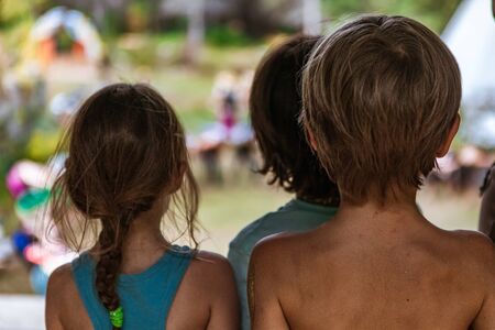 Three innocent children are seen from behind in soft focus during a festival celebrating traditional cultures with blurry people dancing in backgroundの写真素材