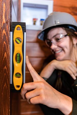 selective focus of spirit level on womans hand, she wore a grey hard hat as she smiling in the...