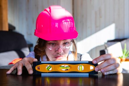 young caucasian woman architect wearing a pink hard hat and protective eyewear, she measuring...
