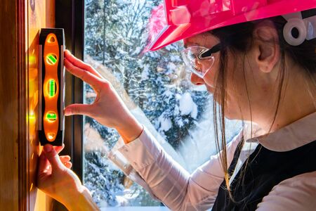 close up on woman architect wearing a pink hard hat and protective glasses using a spirit level on a...