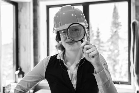 Enlarged eye of construction inspector woman looking through magnifying glass she wearing hard hat during air quality inspection in black and whiteの写真素材