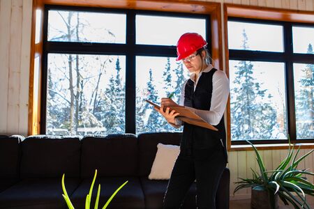 home inspector woman wearing red hard hat takes professional notes on her clipboard during air...