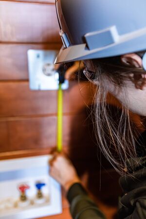 close up and selective focus on inspector woman, as she using a tape to measure the distance between 220v outlet and water valves in the backgroundの写真素材