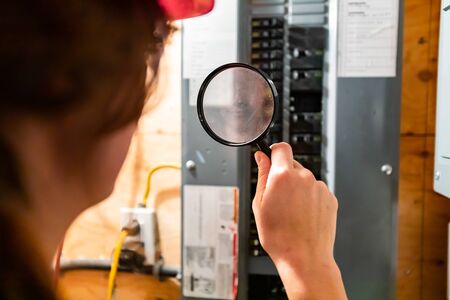 selective focus on inspector womans hand holding a magnifying glass in the front of home Distribution panel board. house electrical systems checkの写真素材