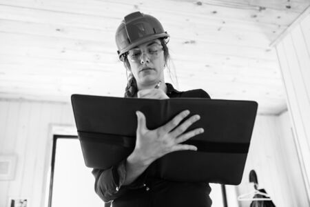 black and white low angle portrait of a home construction inspector woman holding a clipboard as she...
