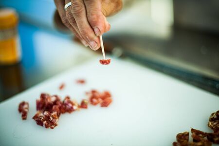 A close up selective focus shot on the hand of a person using a cocktail stick to sample pancetta cured meat at a butchers counter at farmers market.の写真素材