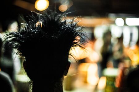 A close up backlit view of a person with a crazy hairstyle seen from behind. Spiky and styled hair silhouette in a club by night with copy space.の写真素材