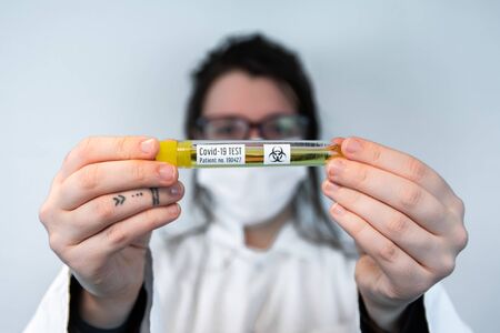 Selective focus shot vial filled with yellow liquid with label Covid-19 test held by tattooed hands...