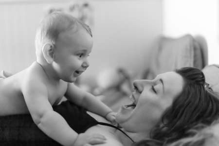 Mother and baby son joyful intimacy. Baby lying on his mothers chest and looking at his mom. Both smiling and laughing. Black and white portrait.の写真素材