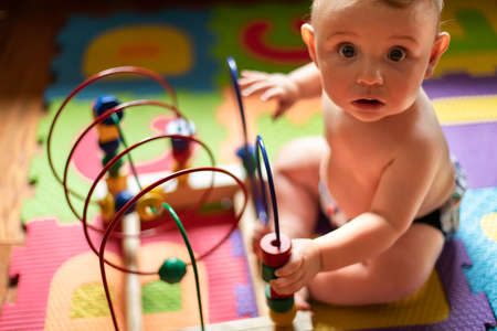 Beautiful, plump baby boy playing with his educational wooden toys made of colors and shapes and looking at camera with funny, surprised expression.の写真素材