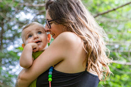 Portrait of a mother and her baby, outdoor in the woods. Mommy is holding her son in her arms. Baby looking up at something while mom fondles him.の写真素材