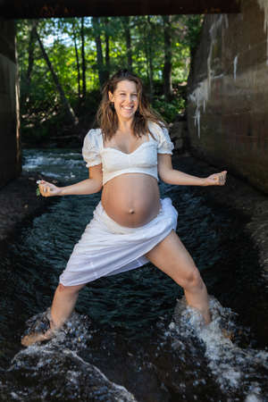 Dynamic, fit and beautiful young pregnant woman with naked belly posing for camera in the bed of a stream, under a bridge. Energy and self confidence.の写真素材