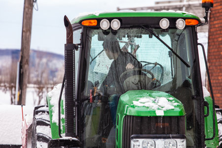 Man driving backwards in a green tractor blowing snow from the streets after a winter storm, low angle viewのeditorial素材