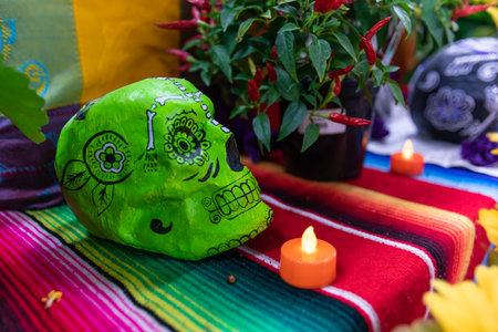 Selective focus of illuminated and electric candle, and decorated green sugar skull on cloth with fresh red chilli plant during celebration of dia de los muertosの写真素材