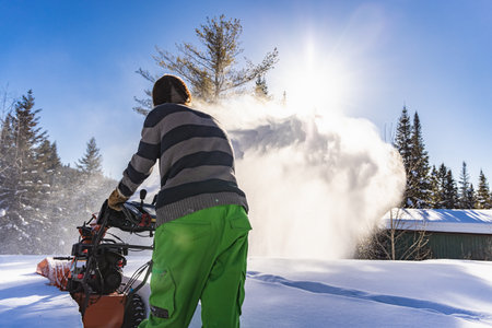 Close up shot of a yong man in yellow fluo pants digging a path in the snow with an orange mechanical snowplough in a sunny winter day in Canada.の写真素材
