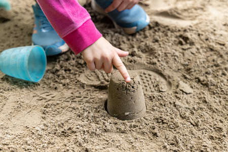 A picture of a child hands, wearing pink jacket and blue joggers, playing on sand while pointing on a sand model, made with a blue mold.の写真素材