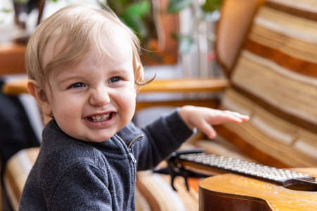 Closeup portrait of a happy smiling three year old caucasian boy playing with a guitar in selective focus with copy space to right.の写真素材
