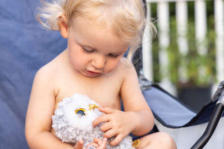 Closeup selective focus view of a cute preschool toddler filling the frame, sitting outdoors and looking down and cuddling a soft plush toy.の写真素材