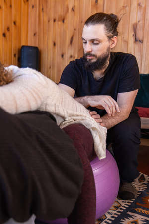 Portrait of a caucasian male Shiatsu practitioner, manipulating the life energy of a female client seen blurred to the left of frame with copy space.の写真素材